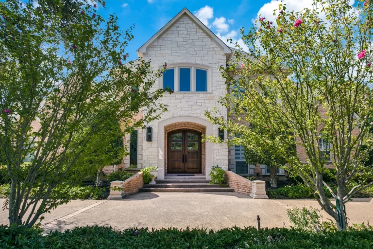 Large stone house with a double wooden door and arched entrance, framed by green trees