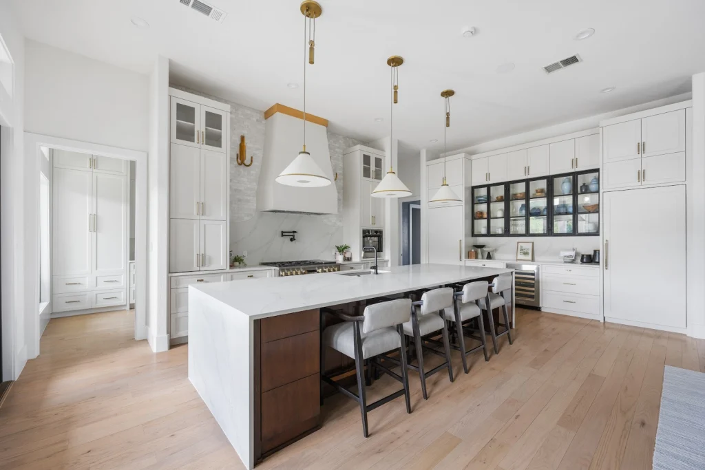 Spacious white kitchen with a large island, gold accents, light wood floors, and display cabinets