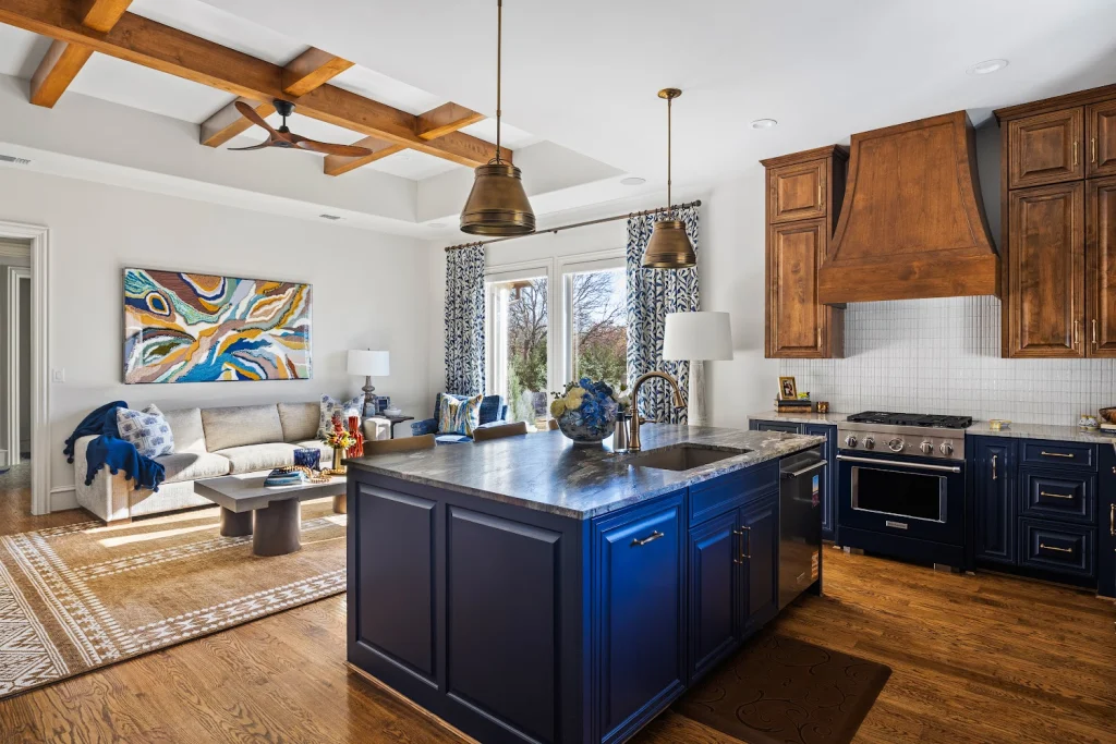 Open-concept kitchen and living area with a navy island, brass pendant lights, wooden range hood, and blue decor accents.